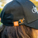 Black cap with a numbat pin and logo on the back, worn by a person outdoors.