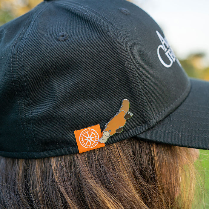 Black cap with orange and platypus pin worn by a person outdoors