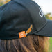 Black cap with orange and platypus pin worn by a person outdoors