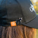 Black cap with a logo and tasmanian devil pin, worn by a person with beautiful hair.