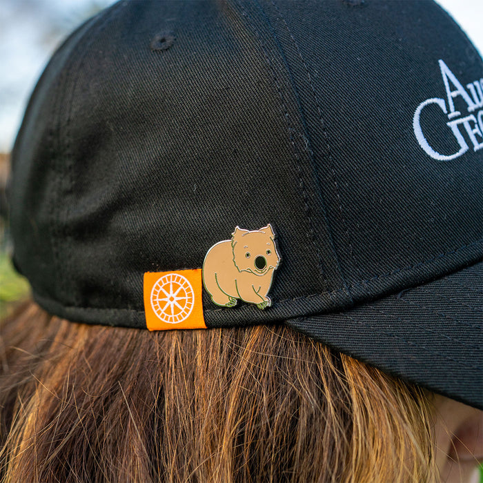 Black cap with a small wombat pin and orange tag worn by a person