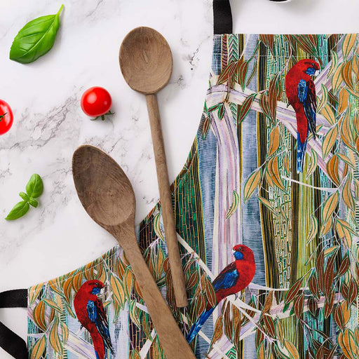Colorful apron with bird design, wooden spoons, and tomatoes on a marble surface