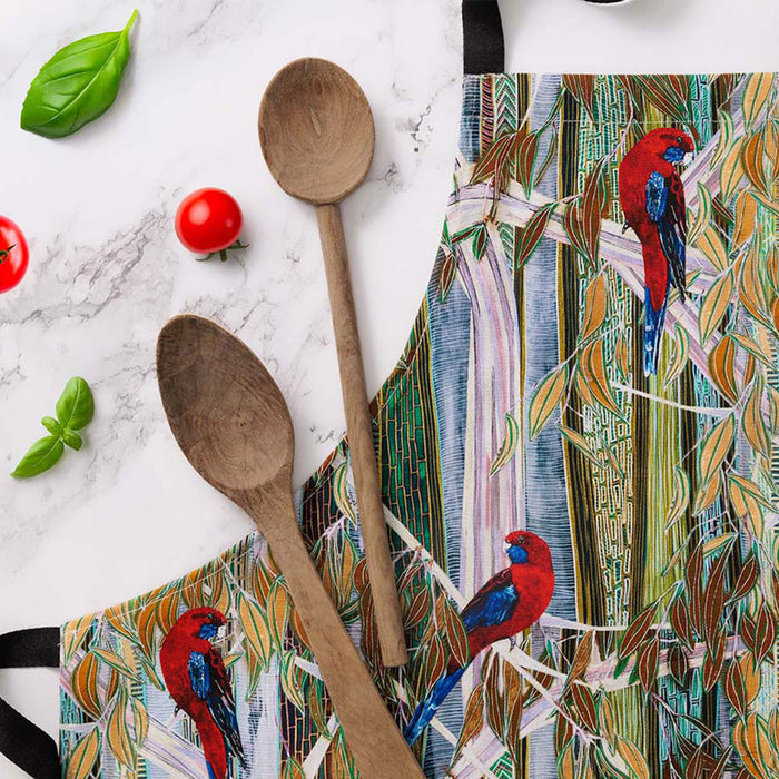 Colorful apron with bird design, wooden spoons, and tomatoes on a marble surface