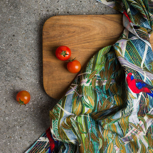 Wooden cutting board with tomatoes and a colorful patterned fabric on a concrete surface