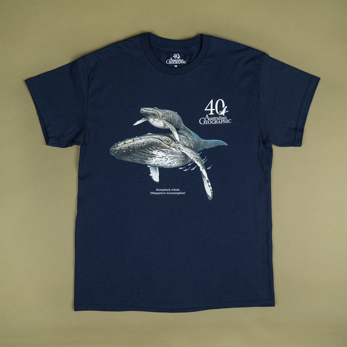 A navy blue short-sleeve t-shirt with a graphic print of a humpback whale and a white '40th Australian Geographic' logo on the chest, laid flat against a solid olive-beige background.