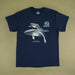 A navy blue short-sleeve t-shirt with a graphic print of a humpback whale and a white '40th Australian Geographic' logo on the chest, laid flat against a solid olive-beige background.