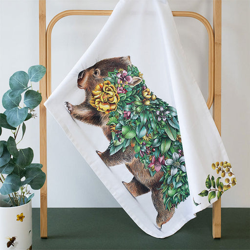 Towel with a wombat design featuring flowers and leaves, hanging on a wooden rack.
